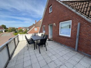 Große Dachterrasse der Ferienwohnung 2 im Haus Vier Nordlichter in Bensersiel mit Tisch, Stühlen und Blick ins Grüne.