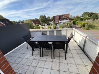 Große Dachterrasse der Ferienwohnung 2 im Haus Vier Nordlichter in Bensersiel mit Tisch, Stühlen und Blick ins Grüne.